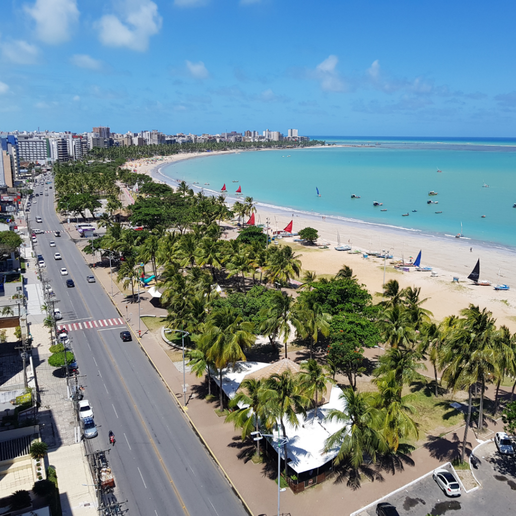 Vista da orla da praia de Maceió, com mar de águas cristalinas e coqueiros ao fundo
