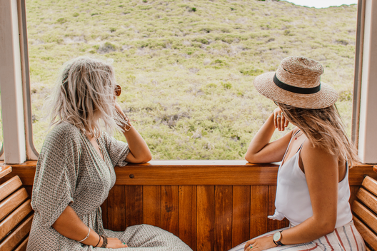 Duas mulheres contemplando uma paisagem montanhosa durante uma viagem, transmitindo liberdade e conexão com a natureza